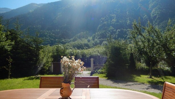 Une table entourée de chaises, sur laquelle est posé un vase de fleurs, le tout se détachant sur un paysage montagneux en arrière-plan.