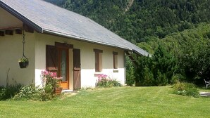 Un bâtiment d’un seul étage, doté d’un toit en pente, d’un porche à l’avant avec des volets en bois et d’un pot à fleurs suspendu.