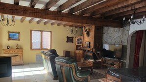 Un salon spacieux avec un plafond haut, des poutres apparentes, une cheminée et un téléviseur.