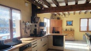 Une cuisine avec des meubles en bois, un lave-vaisselle et une cuisinière. Il y a des fenêtres avec des rideaux, un lustre et une vue sur l’extérieur.
