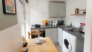A compact kitchen with white cabinets, a microwave, a washing machine, and a dining area with a table set for two. - £ - City Centre - Duke Street Studio ~ 5* Location (Liverpool)