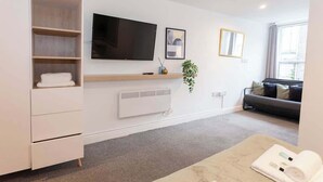 A modern hotel room with a flat-screen TV, a sofa, a coffee table, a plant, and a large window. - £ - City Centre - Duke Street Studio ~ 5* Location (Liverpool)