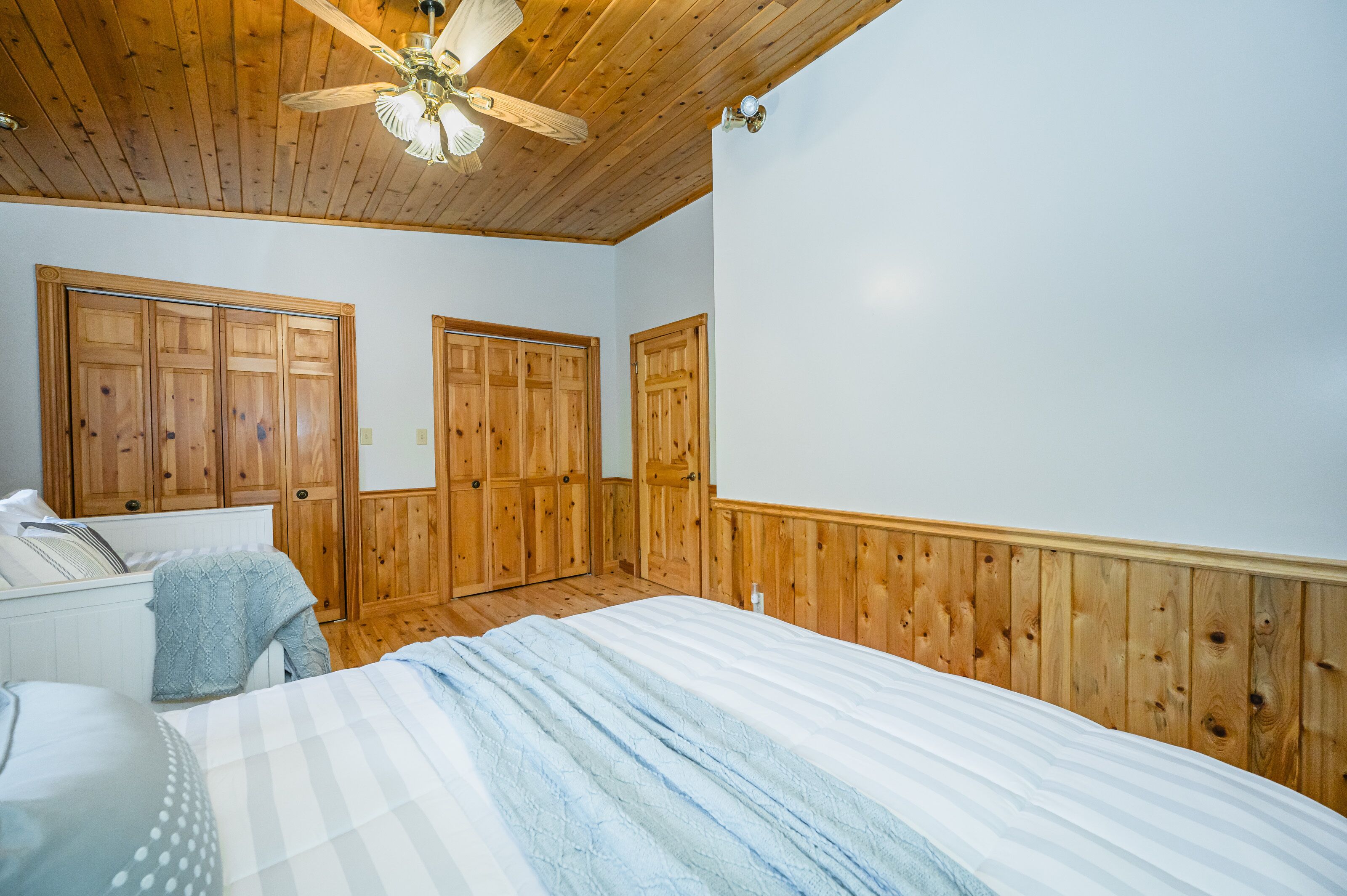 Ein Schlafzimmer mit Holzwandverkleidung, Deckenventilator und einem Bett mit gestreifter Decke.