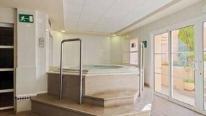 Ein Wellnessbereich mit Whirlpool, einer Metallbank und einer Glastür, die nach draußen führt.