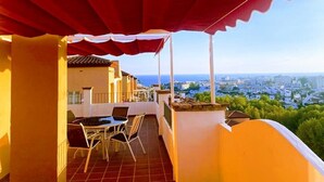 Een balkon met een rood luifel, een tafel met stoelen, en uitzicht op de stad en zee.