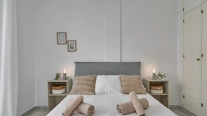 Een netjes opgemaakt bed met twee kussens, twee nachtkastjes met lampen en een kledingkast.