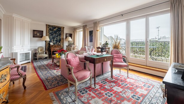 A spacious room with a large window, a wooden floor, and a red patterned rug.