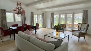 Un salon spacieux avec un grand canapé, une table à manger et des chaises, ainsi qu’un lustre.