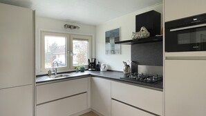 Une cuisine moderne avec des meubles blancs, un plan de travail noir, une cuisinière et une fenêtre donnant sur l’extérieur.