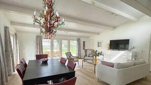 Un vaste salon comprenant un coin repas, un canapé blanc, un téléviseur et un lustre.