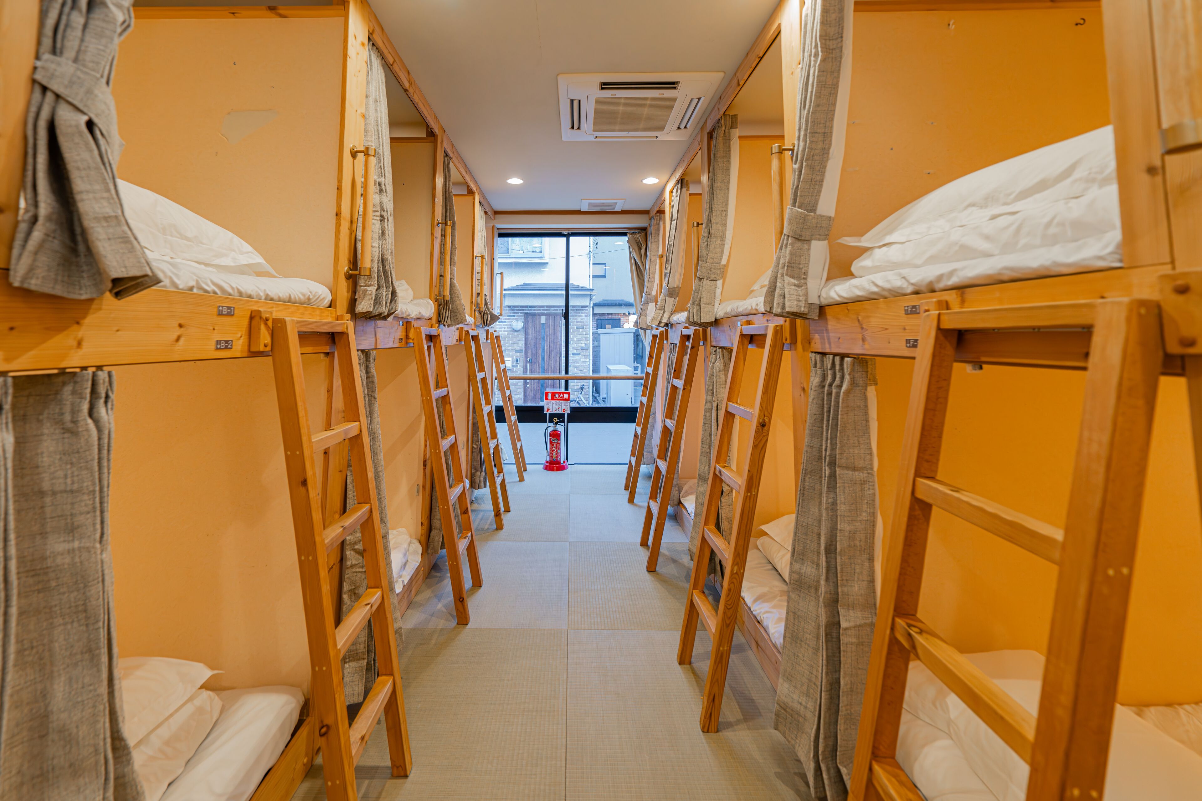 A corridor with bunk beds, a fire extinguisher, and a window at the end.