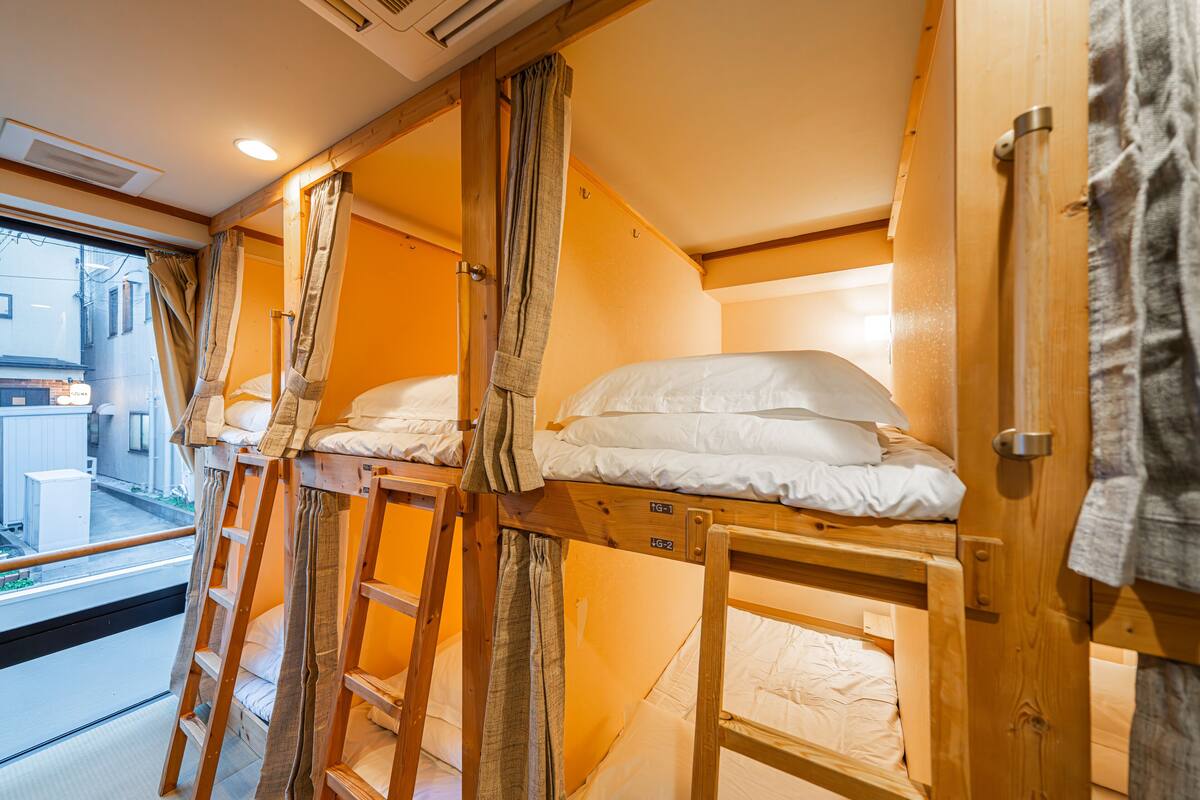 A compact room with bunk beds and a ladder, wooden walls, and a window with curtains.
