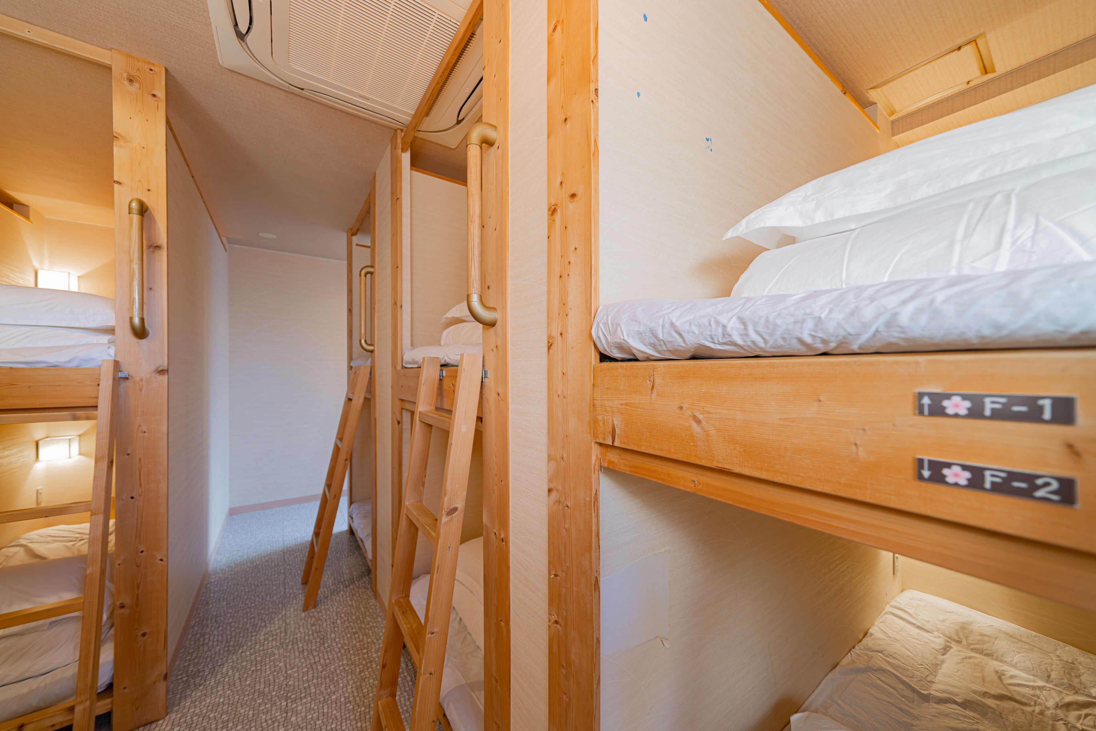 A compact, wooden bunk room with two labeled beds, F-1 and F-2, and a ladder for access.