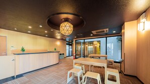A modern interior with a wooden reception desk, a large table with benches, and a geometric ceiling light.