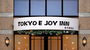 The exterior of Tokyo E Joy Inn with a large entrance, snowflake decorations, and a small Christmas tree.