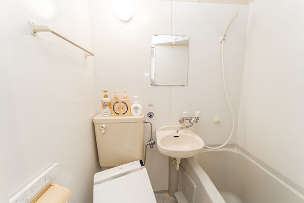 A small, clean bathroom with a toilet, sink, and bathtub. There are toiletries on the toilet tank. - 11Capsules (E JOY INN East Nippori Branch) (Tokyo)