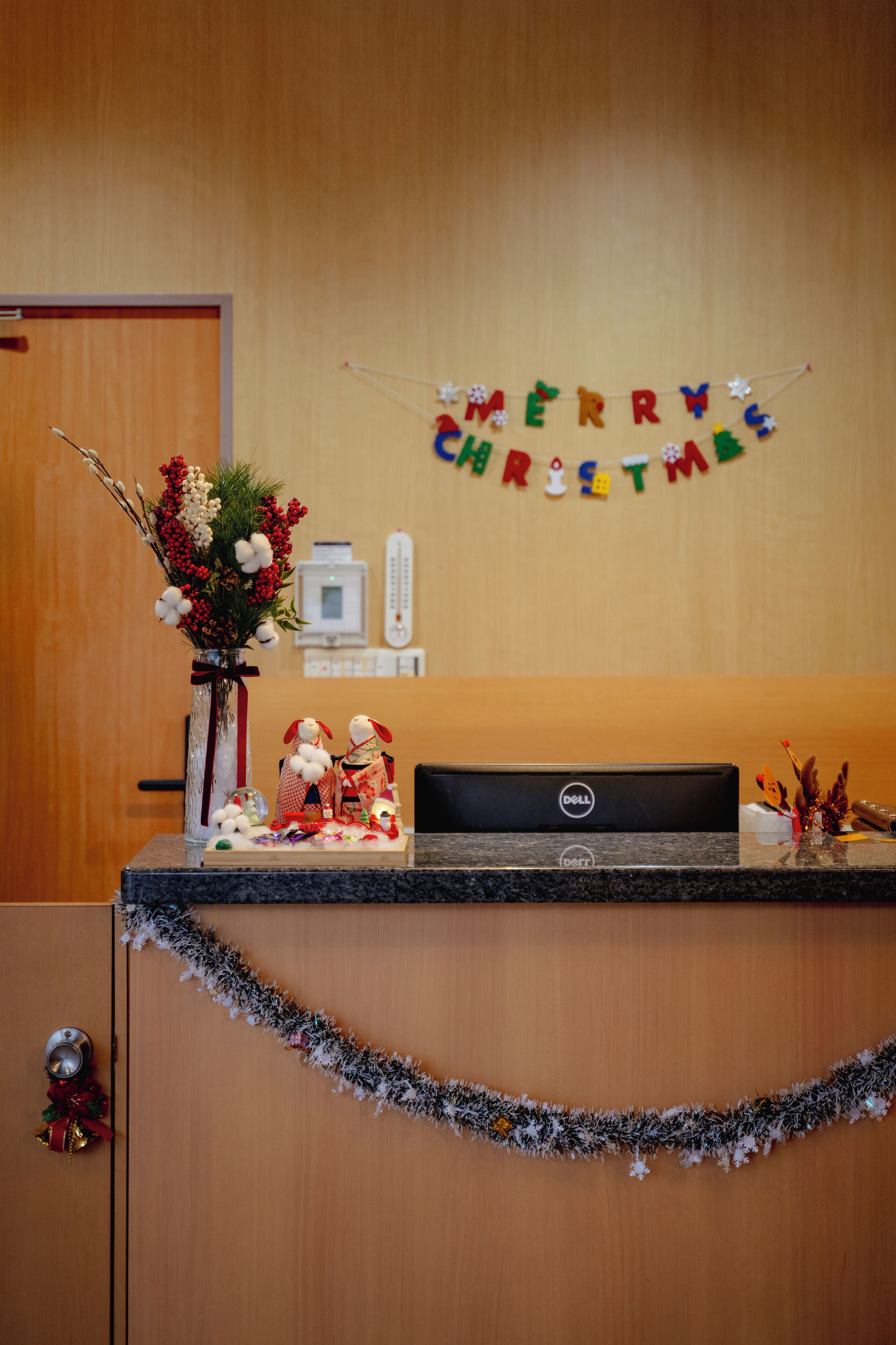 A reception desk with a 'MERRY CHRISTMAS' banner, a vase with flowers, and a computer.
