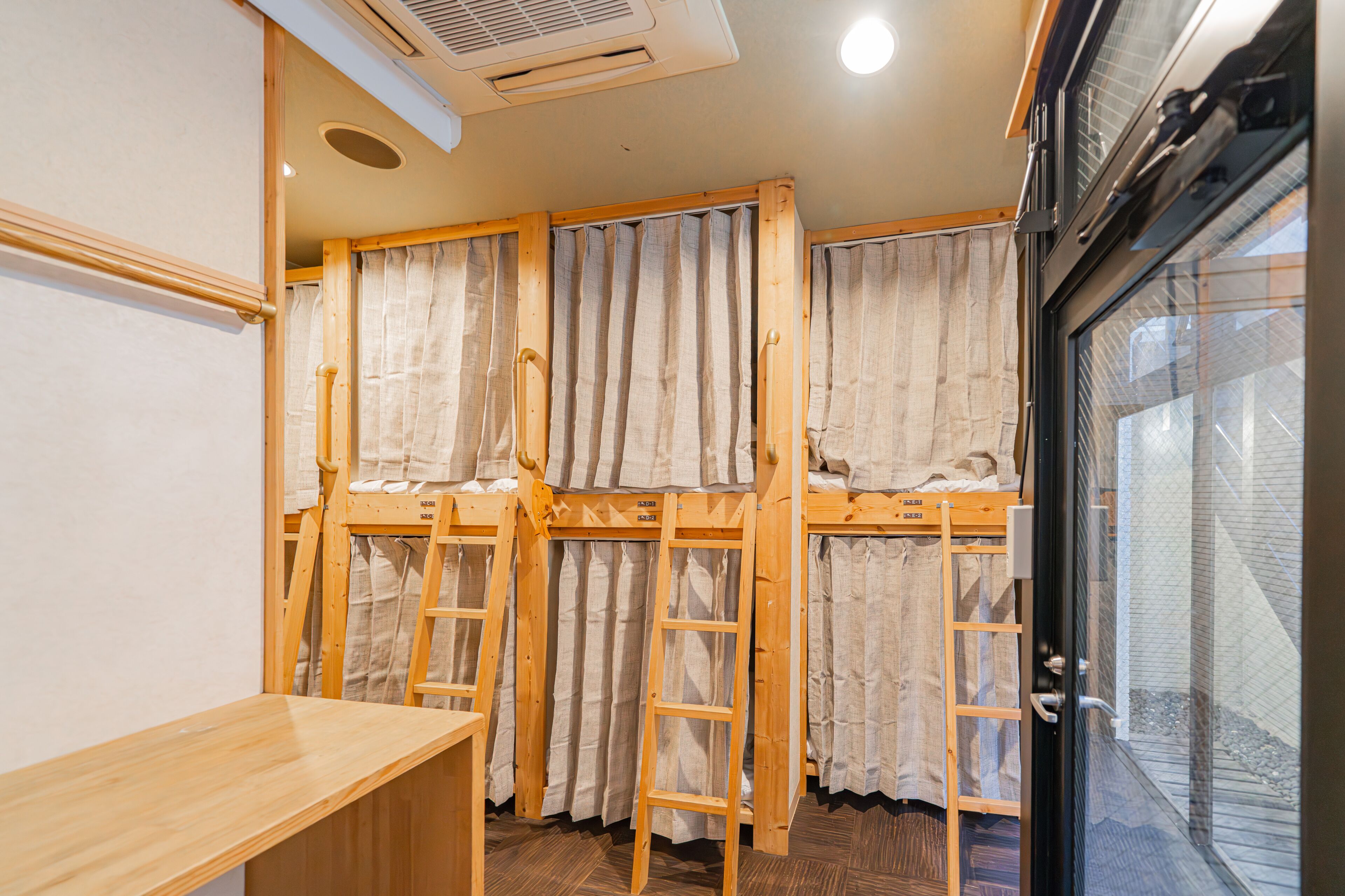A dormitory room with bunk beds, wooden ladders, and curtains.