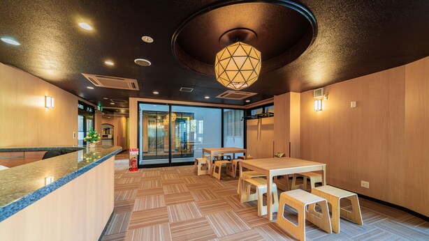 A modern interior with a reception desk, wooden flooring, and a dining area with tables and benches.