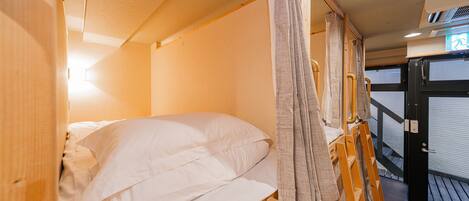 A compact, single-bed room with a wooden bunk bed structure, a small window, and a door leading outside.