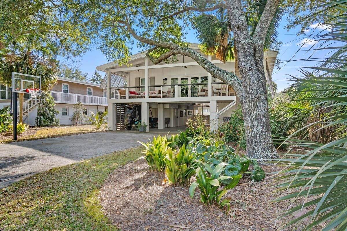A two-story house with a balcony, surrounded by tropical plants and a basketball hoop.