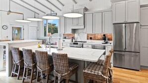 Een moderne keuken met een groot kookeiland, roestvrijstalen apparatuur en rieten barkrukken.