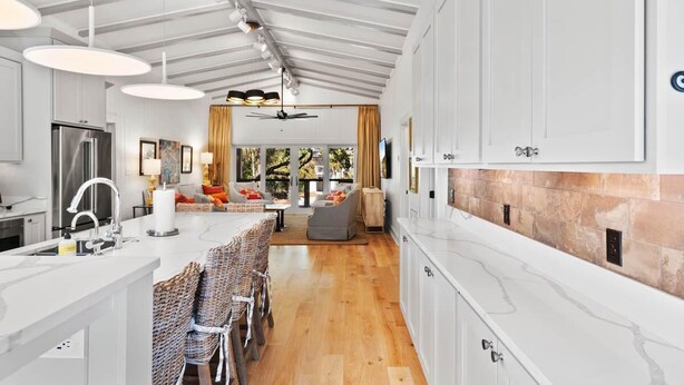Een moderne keuken met witte kasten, een centraal eiland met zitplaatsen, en een eethoek met rieten stoelen.
