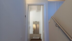 Een smalle gang die leidt naar een badkamer met een wastafel en spiegel.