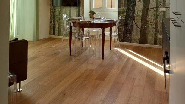 Een eethoek met een houten tafel en stoelen, een aan de muur bevestigde televisie en een groot raam met uitzicht op een bos.