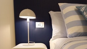A neatly made bed with striped bedding, a white bedside table with a lamp, and a power outlet on the wall. - Ca'Foulard3: a dip in the blue (Cernusco sul Naviglio)