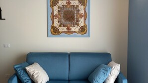 A room with a blue sofa, a decorative wall piece, and exposed wooden beams. - Ca'Foulard3: a dip in the blue (Cernusco sul Naviglio)
