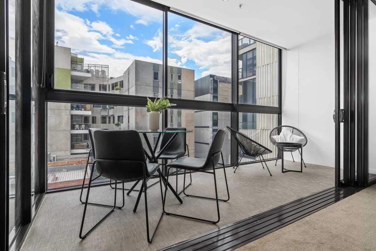 A modern room with a large window, a dining table with chairs, and a small seating area with a chair and a plant.