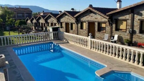 Zona de piscina amb edificis de pedra, una tanca blanca i un cel serè.