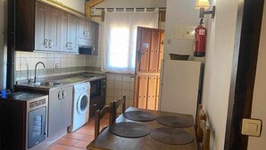 A compact kitchen with a washing machine, a dining table with placemats, and a fire extinguisher mounted on the wall. - [5] (Zarza De Granadilla)