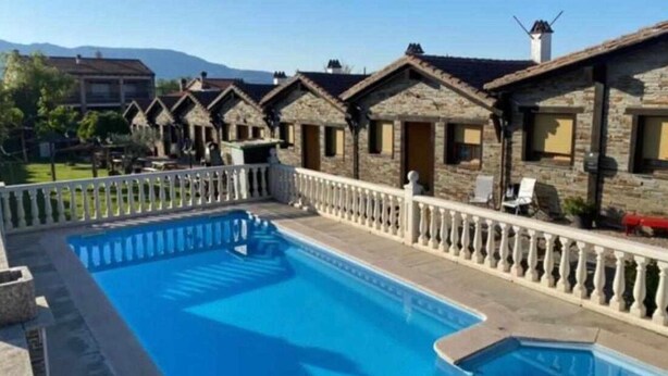 A pool area with stone buildings, a white fence, and a clear sky. - [5] (Zarza De Granadilla)