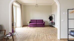 A living room with a purple sofa, a small table with a vase, and a wooden floor. - Colosseo Road by Hili  (Rome)