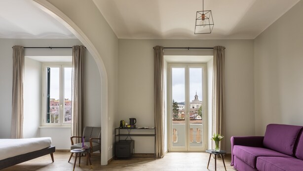 A modern room with a bed, a desk, a purple sofa, and a view of the city through large windows. - Colosseo Road by Hili  (Rome)