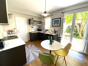 A compact kitchen with a dining area, a small table, and chairs, and a view of the garden through a sliding door.