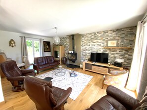 Ein Wohnzimmer mit Sofa, Sesseln, Fernseher, Kamin und einer Steinwand.
