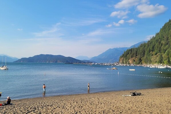 A beach with a calm sea, boats, and mountains in the background.