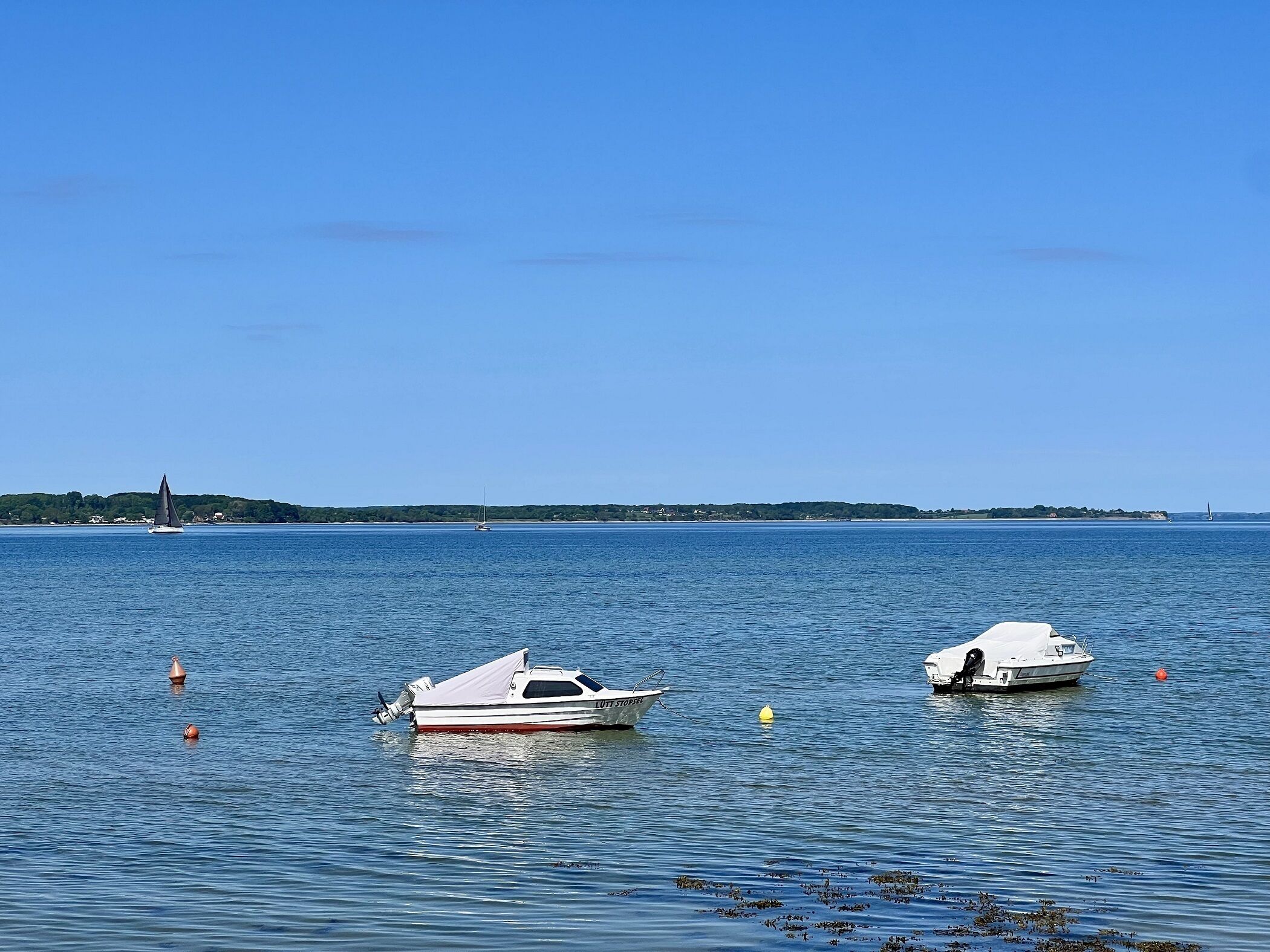 Zwei Boote liegen in ruhigem Wasser vor einer klaren Küstenlinie, der Himmel ist wolkenlos.