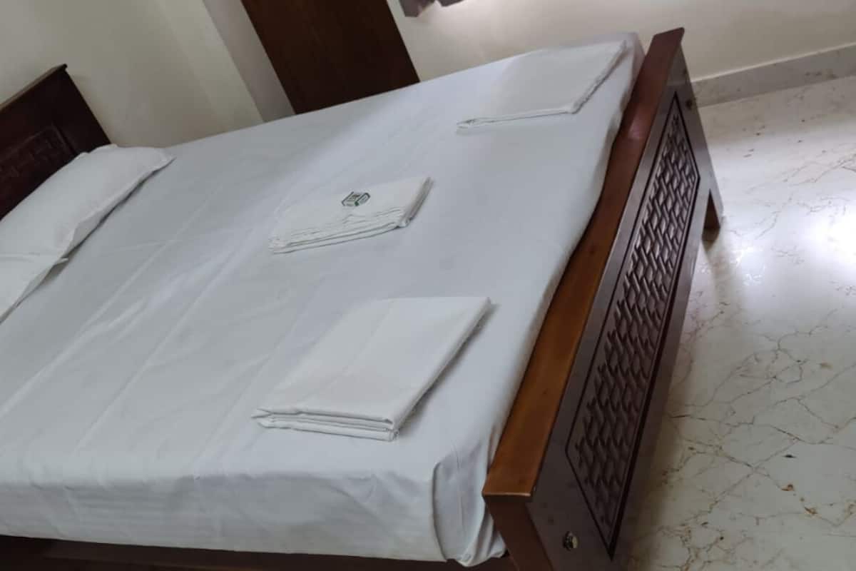 A neatly made bed with white linens and towels, a wooden headboard, and a marble floor.