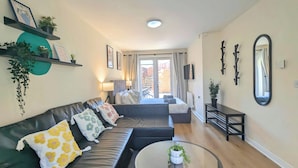 A modern living room with a sofa, a round coffee table, and a TV mounted on the wall. - Spacious 4-bedroom, 3-bath property close to Liverpool city centre, featuring a fully equipped kitchen, bright living room, garden, and free on-street parking. Perfect for families, contractors, or groups seeking comfort and convenience. (Merseyside)