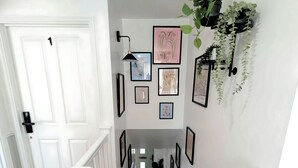 A hallway with a white door, black-framed pictures, a black wall-mounted lamp, and green plants. - Spacious 4-bedroom, 3-bath property close to Liverpool city centre, featuring a fully equipped kitchen, bright living room, garden, and free on-street parking. Perfect for families, contractors, or groups seeking comfort and convenience. (Merseyside)