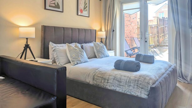 A modern bedroom with a large bed, two bedside lamps, and a view of the outside. - Spacious 4-bedroom, 3-bath property close to Liverpool city centre, featuring a fully equipped kitchen, bright living room, garden, and free on-street parking. Perfect for families, contractors, or groups seeking comfort and convenience. (Merseyside)