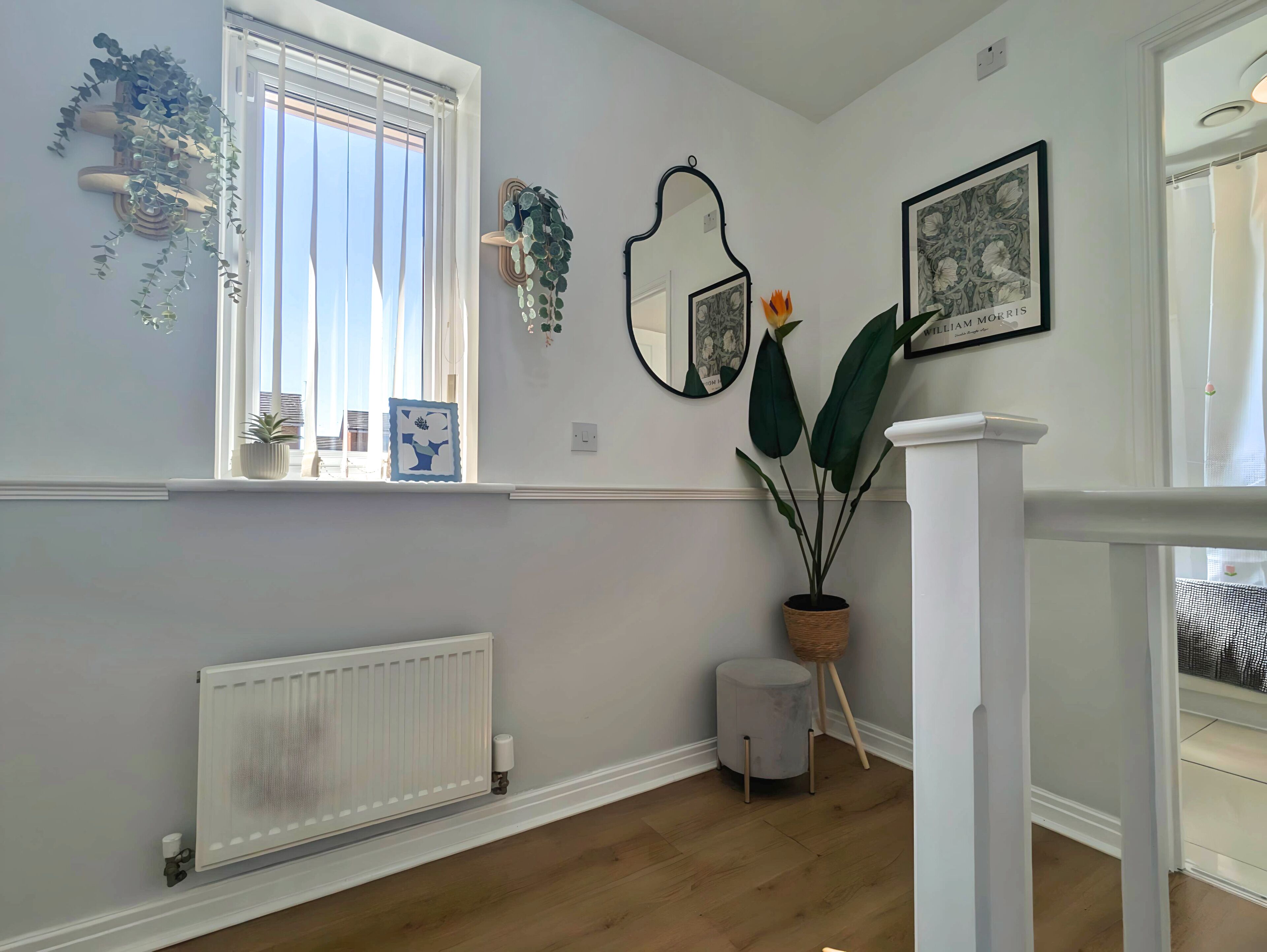 Une pièce avec une fenêtre, un radiateur, un plancher en bois et une rambarde blanche.