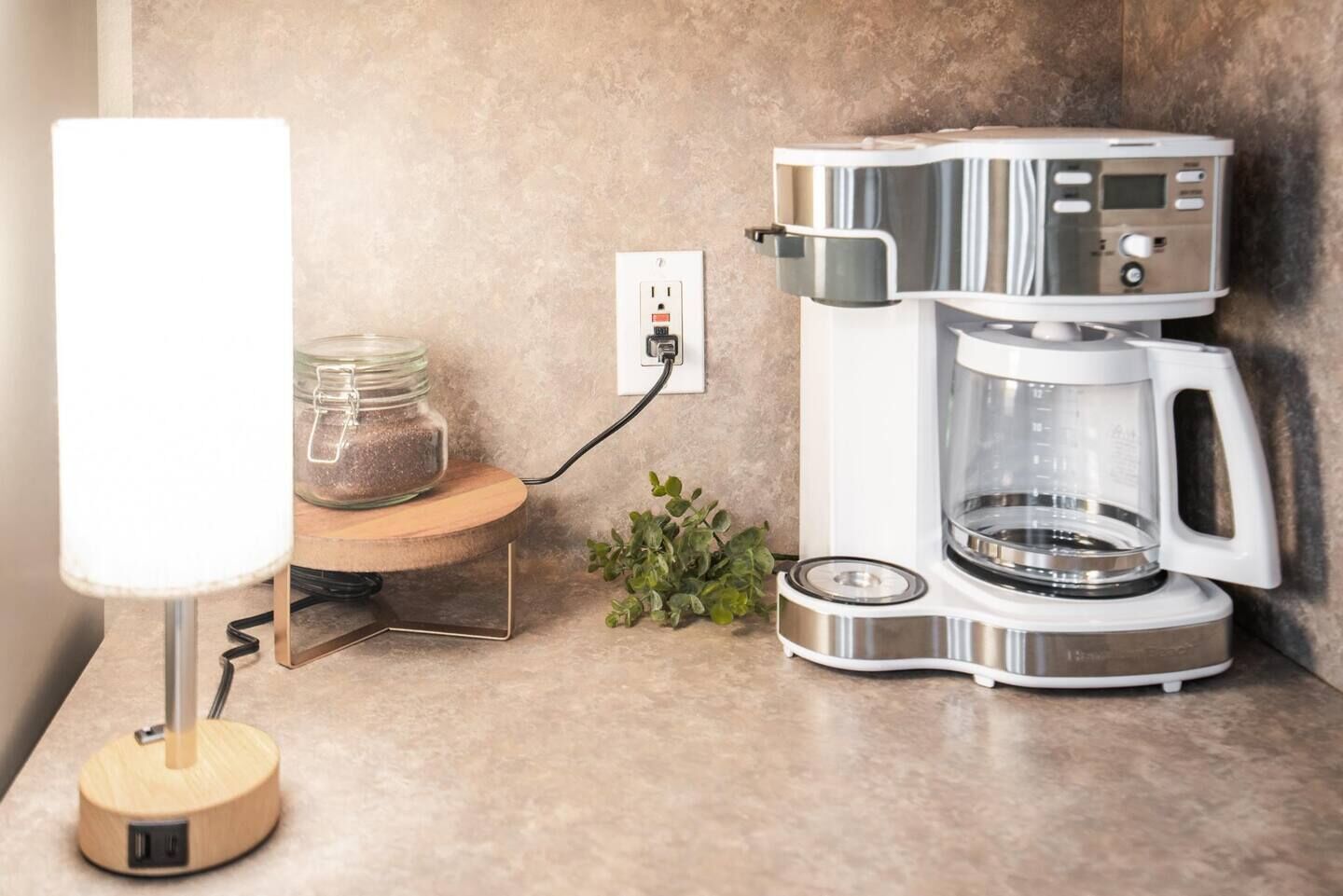 Una cocina con una cafetera, una lámpara y un tarro de azúcar sobre la encimera.