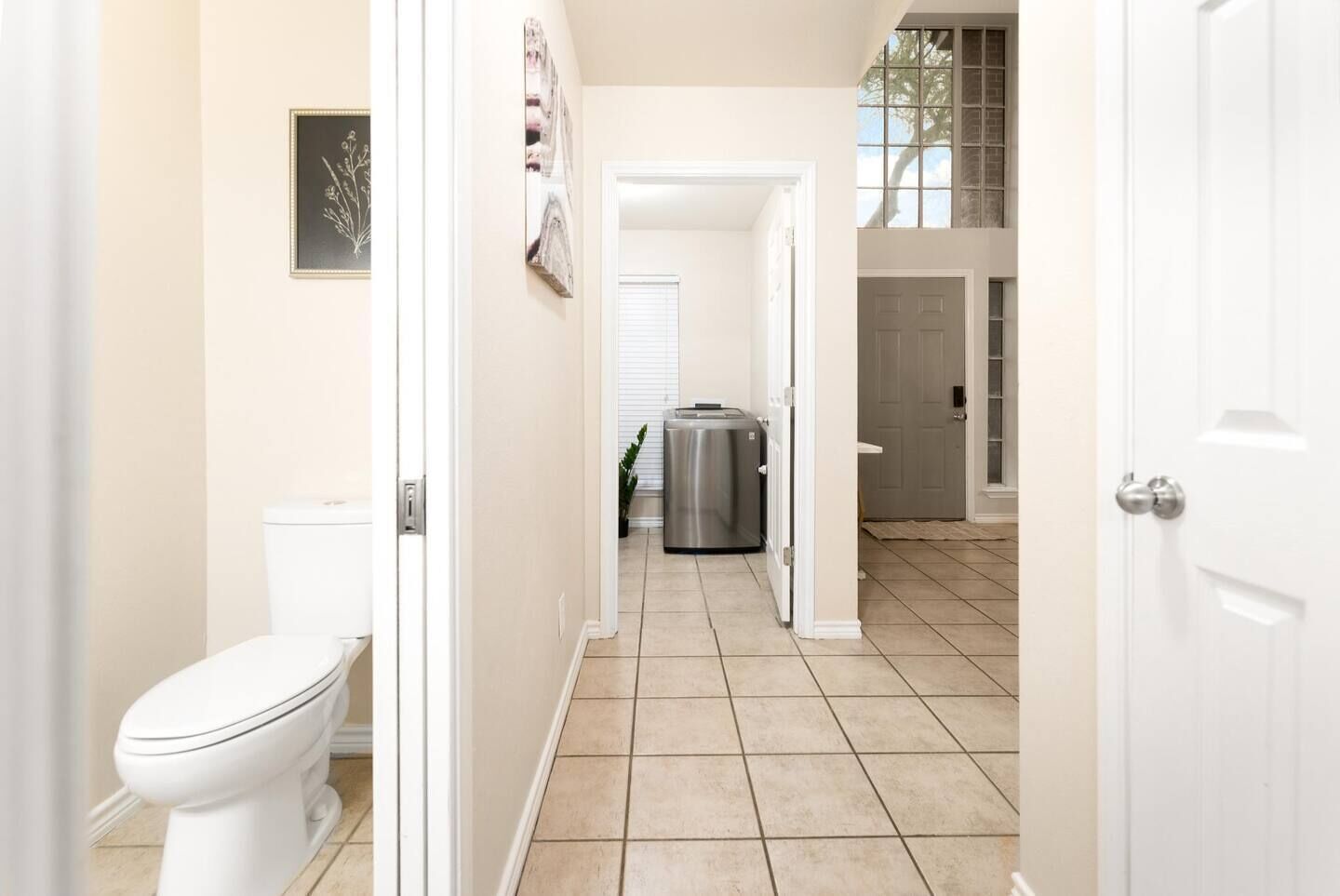 Un couloir avec des toilettes, une poubelle en acier inoxydable et une porte donnant sur une autre pièce.