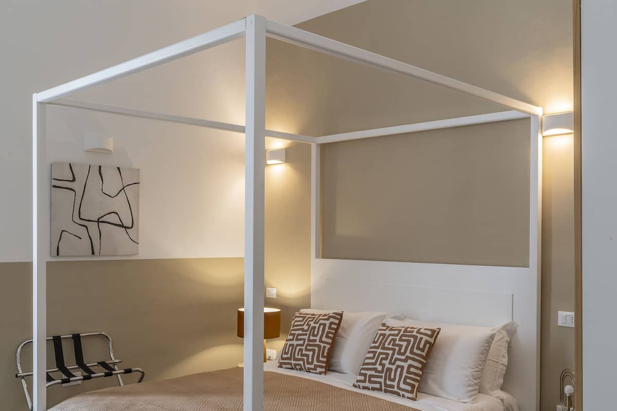 Un lit à baldaquin avec une tête de lit beige, deux coussins à motifs et une table de chevet avec une lampe.