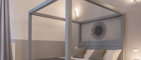 A modern bedroom with a four-poster bed, a geometric wall art piece, and a bedside table with a lamp.